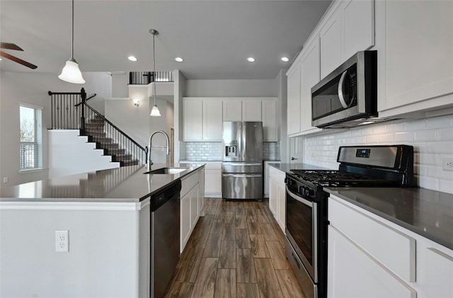 kitchen featuring appliances with stainless steel finishes, a kitchen island with sink, sink, white cabinetry, and hanging light fixtures