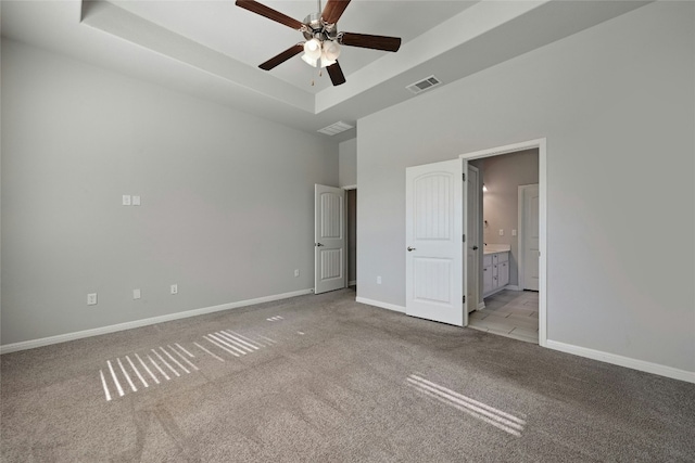 unfurnished bedroom with ceiling fan, a raised ceiling, light carpet, and ensuite bath