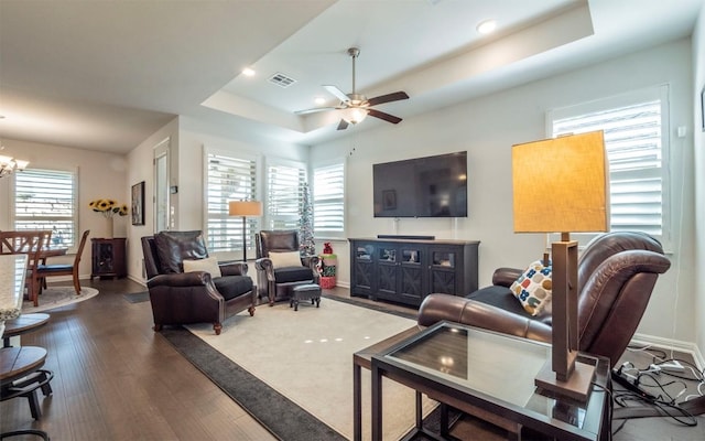 living room featuring dark hardwood / wood-style floors, ceiling fan with notable chandelier, and a raised ceiling