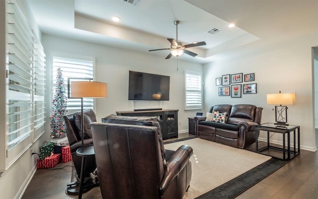 living room featuring dark hardwood / wood-style floors, ceiling fan, and a tray ceiling