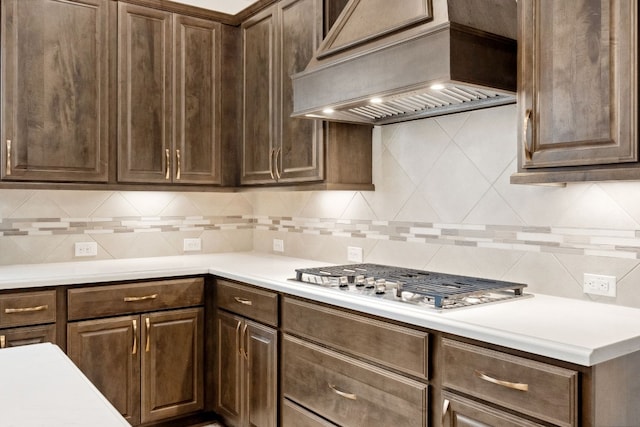 kitchen with custom range hood, tasteful backsplash, stainless steel gas cooktop, and dark brown cabinets