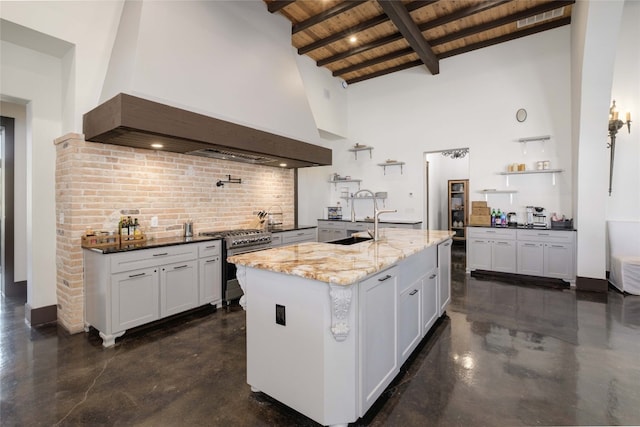 kitchen with custom range hood, high end stove, a center island with sink, wooden ceiling, and white cabinets