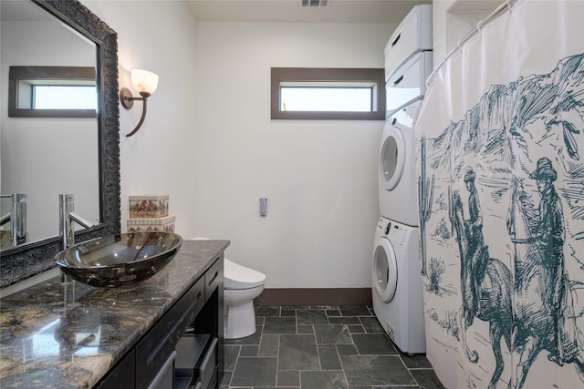 bathroom featuring a healthy amount of sunlight, vanity, toilet, and stacked washer and clothes dryer