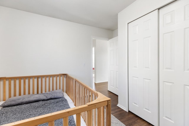 bedroom featuring a nursery area, dark wood-type flooring, and a closet