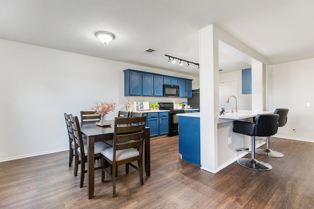 kitchen with dark wood-type flooring, blue cabinetry, black appliances, a kitchen bar, and kitchen peninsula