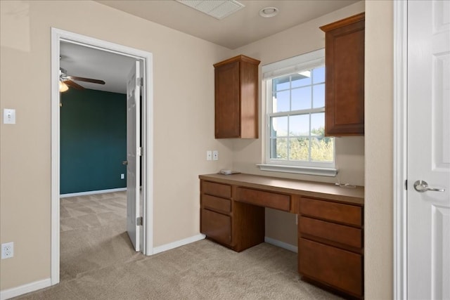 unfurnished office with light colored carpet, visible vents, built in study area, ceiling fan, and baseboards