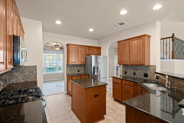 kitchen featuring appliances with stainless steel finishes, dark stone counters, sink, light tile patterned floors, and a kitchen island