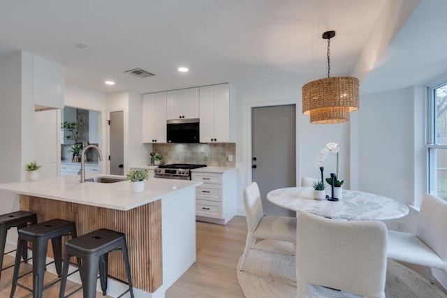 kitchen with white cabinets, sink, hanging light fixtures, an island with sink, and stainless steel appliances