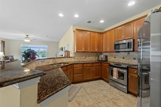 kitchen with appliances with stainless steel finishes, kitchen peninsula, sink, and dark stone countertops