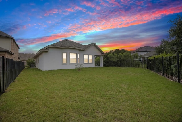 back house at dusk featuring a lawn