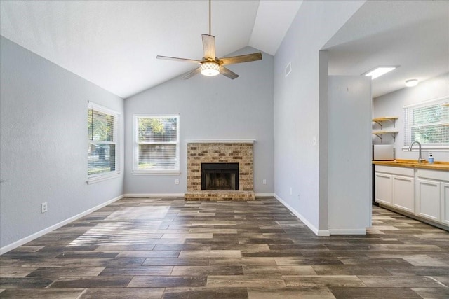 unfurnished living room featuring dark hardwood / wood-style flooring, lofted ceiling, a wealth of natural light, and a brick fireplace