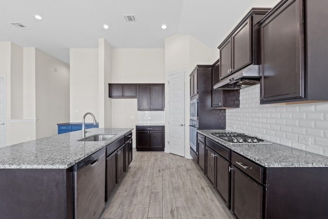 kitchen with appliances with stainless steel finishes, light stone counters, a kitchen island with sink, and sink