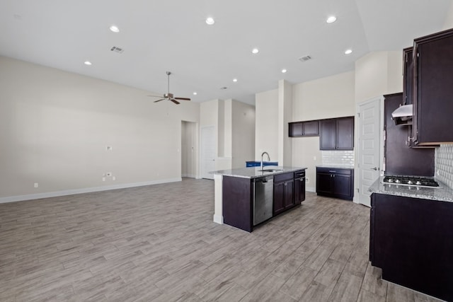 kitchen with decorative backsplash, stainless steel appliances, sink, light hardwood / wood-style flooring, and an island with sink