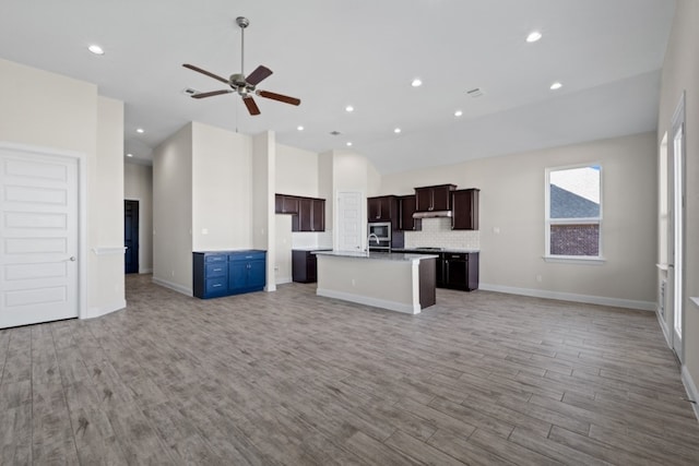 kitchen with ceiling fan, decorative backsplash, light wood-type flooring, and an island with sink