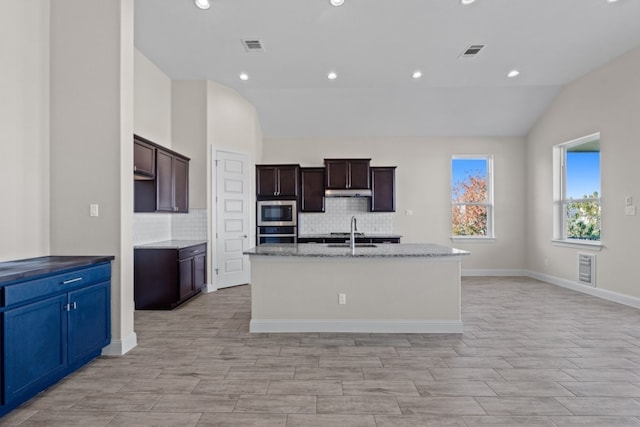 kitchen featuring backsplash, a kitchen island with sink, lofted ceiling, and appliances with stainless steel finishes