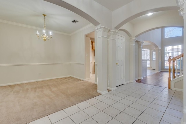 carpeted empty room with ornate columns, crown molding, and an inviting chandelier