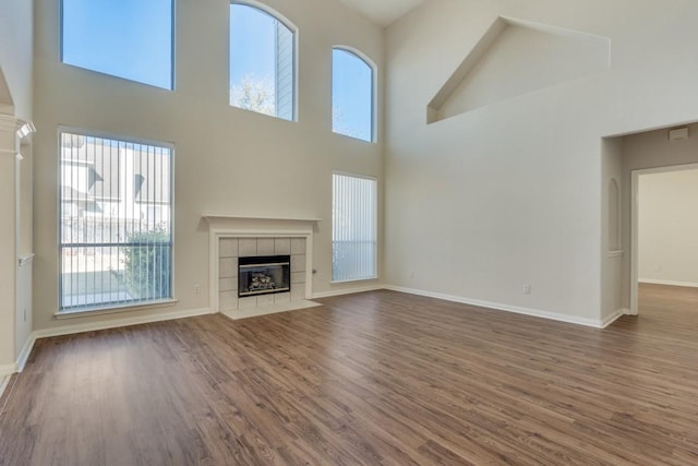 unfurnished living room with a tiled fireplace, a high ceiling, and hardwood / wood-style flooring