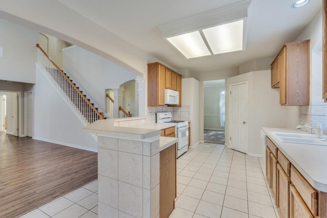 kitchen featuring kitchen peninsula, light wood-type flooring, tasteful backsplash, white appliances, and sink