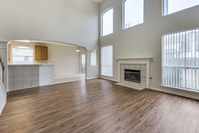 712 Runners Rdg, Pflugerville, TX 78660 - unfurnished living room featuring light wood-style flooring, a high ceiling, a tiled fireplace, arched walkways, and decorative columns