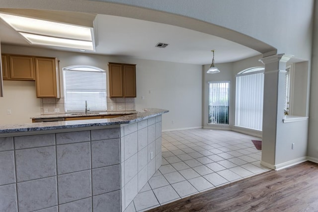 712 Runners Rdg, Pflugerville, TX 78660 - kitchen featuring decorative backsplash, light stone counters, ornate columns, decorative light fixtures, and light wood finished floors