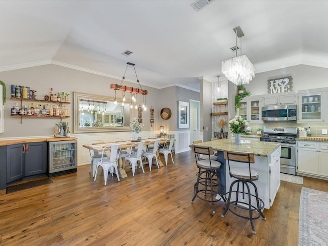 kitchen with wine cooler, appliances with stainless steel finishes, a kitchen bar, white cabinets, and hardwood / wood-style flooring