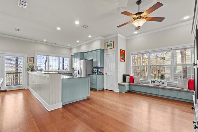 kitchen with kitchen peninsula, stainless steel fridge, ceiling fan, crown molding, and light hardwood / wood-style floors