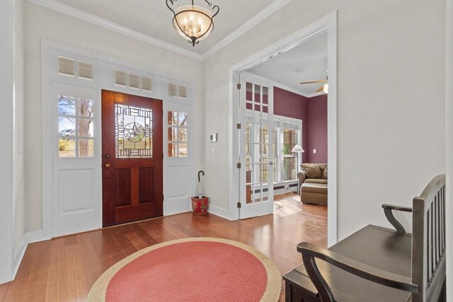 foyer entrance with a wealth of natural light, hardwood / wood-style floors, ceiling fan with notable chandelier, and ornamental molding