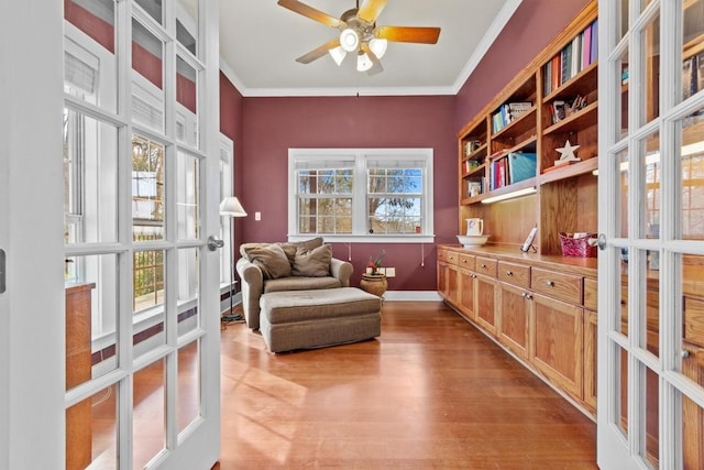 living area featuring light wood-type flooring, ornamental molding, a ceiling fan, and french doors