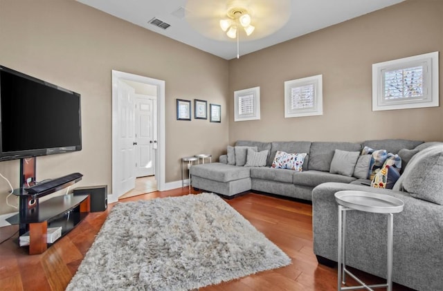 living room featuring a ceiling fan, visible vents, baseboards, and wood finished floors