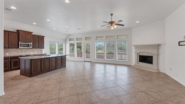 kitchen with a high end fireplace, backsplash, ceiling fan, a center island with sink, and light tile patterned flooring