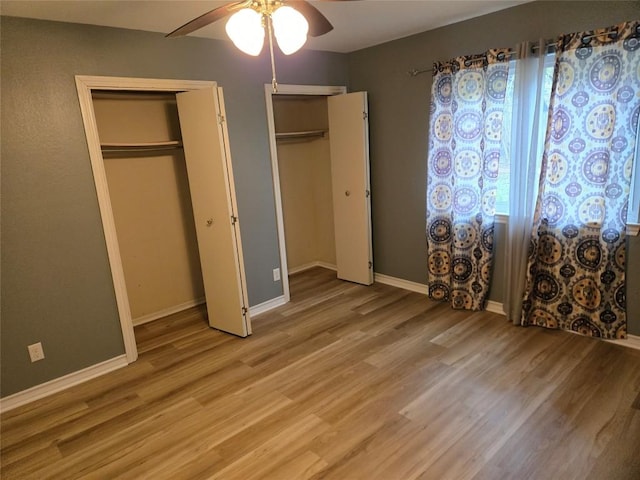 unfurnished bedroom with ceiling fan, two closets, and hardwood / wood-style flooring