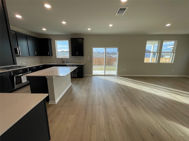 kitchen featuring appliances with stainless steel finishes, a kitchen island, sink, backsplash, and light wood-type flooring