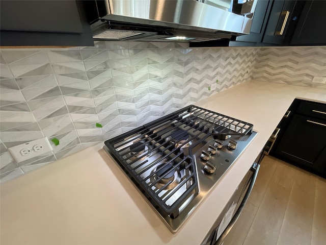 kitchen with decorative backsplash, stainless steel gas stovetop, ventilation hood, and light wood-type flooring