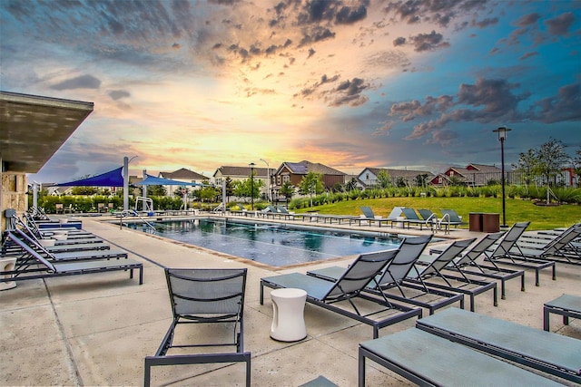 pool at dusk featuring a patio, a lawn, and a community pool