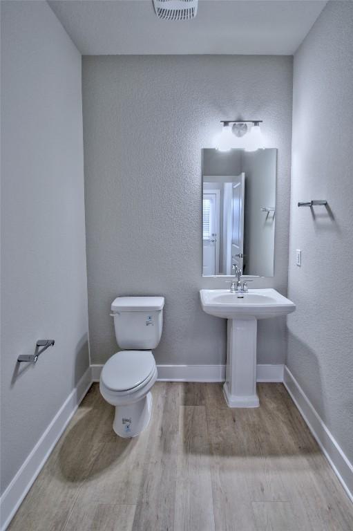 half bath with toilet, baseboards, visible vents, and wood finished floors