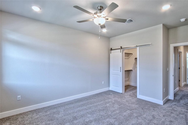 unfurnished bedroom featuring a barn door, visible vents, baseboards, a walk in closet, and carpet floors