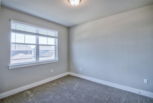 spare room featuring dark colored carpet and baseboards