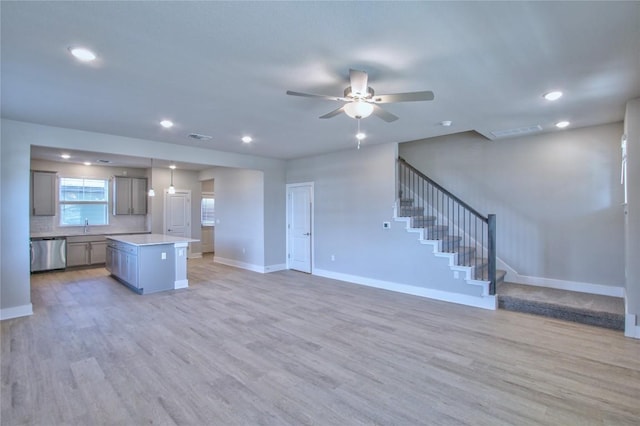 kitchen with a center island, gray cabinets, stainless steel dishwasher, open floor plan, and light wood-type flooring