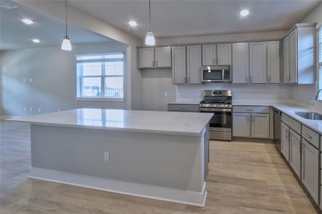 kitchen featuring appliances with stainless steel finishes, a sink, a center island, and gray cabinetry