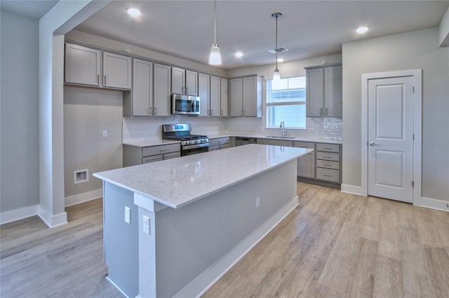 kitchen with sink, hanging light fixtures, stainless steel appliances, light stone countertops, and a kitchen island