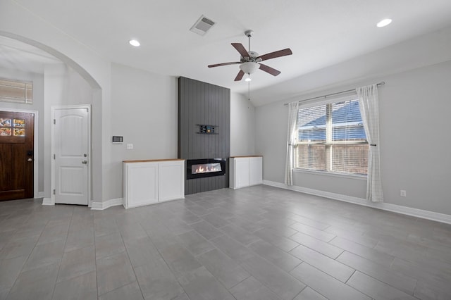 unfurnished living room featuring a large fireplace, baseboards, visible vents, and arched walkways