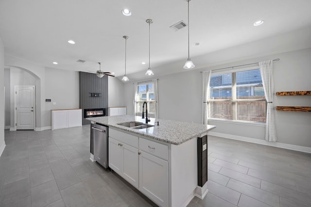 kitchen with light stone countertops, a kitchen island with sink, sink, white cabinets, and hanging light fixtures