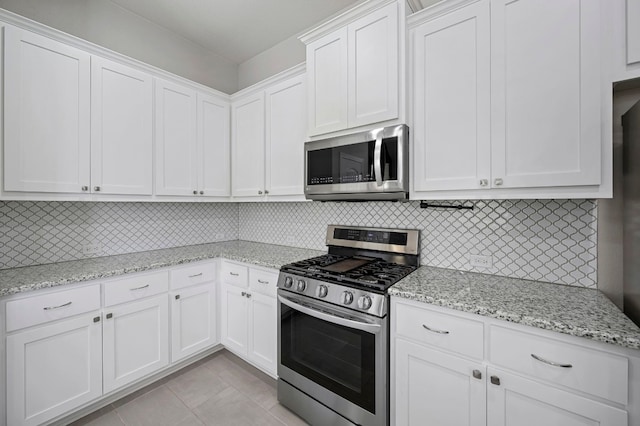 kitchen with light stone countertops, stainless steel appliances, light tile patterned floors, backsplash, and white cabinets