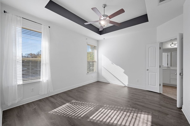 empty room featuring dark wood-style floors, ceiling fan, a raised ceiling, and baseboards