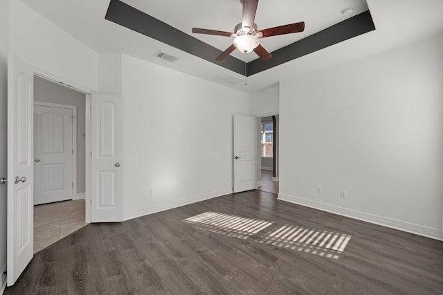 unfurnished room with a tray ceiling, visible vents, dark wood finished floors, and baseboards