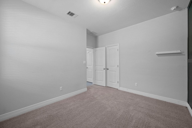 unfurnished bedroom with a textured ceiling, carpet, visible vents, and baseboards