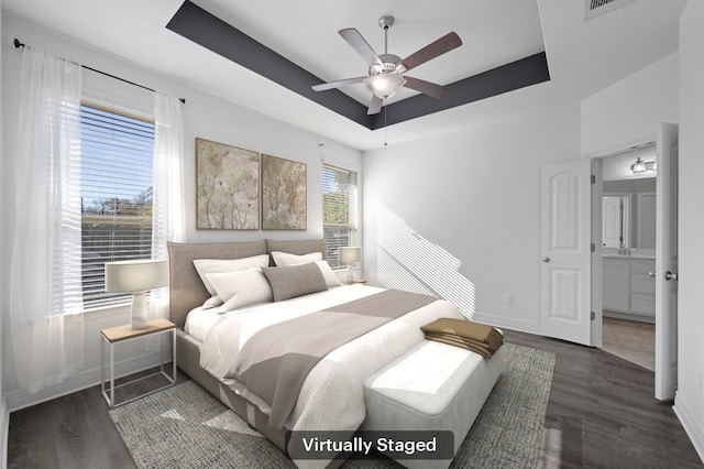 bedroom featuring a raised ceiling, connected bathroom, ceiling fan, and dark wood-type flooring