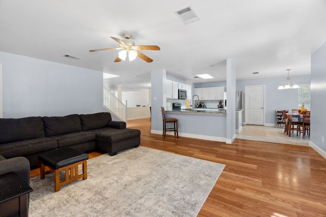 living room with ceiling fan with notable chandelier, sink, and light hardwood / wood-style flooring