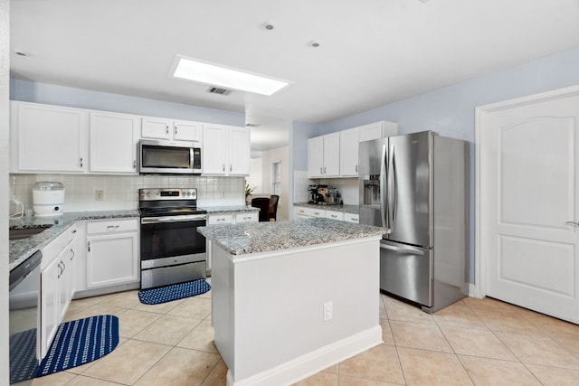 kitchen with light stone countertops, appliances with stainless steel finishes, backsplash, a center island, and white cabinetry