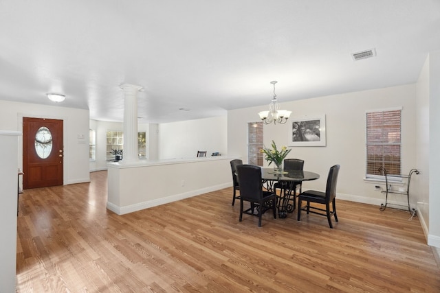 dining room featuring decorative columns, light hardwood / wood-style flooring, and an inviting chandelier